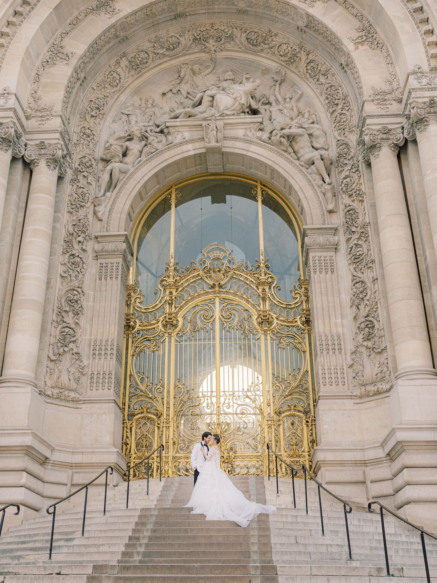 A wedding dress silhouette against ornate golden gates and grand stone architecture.