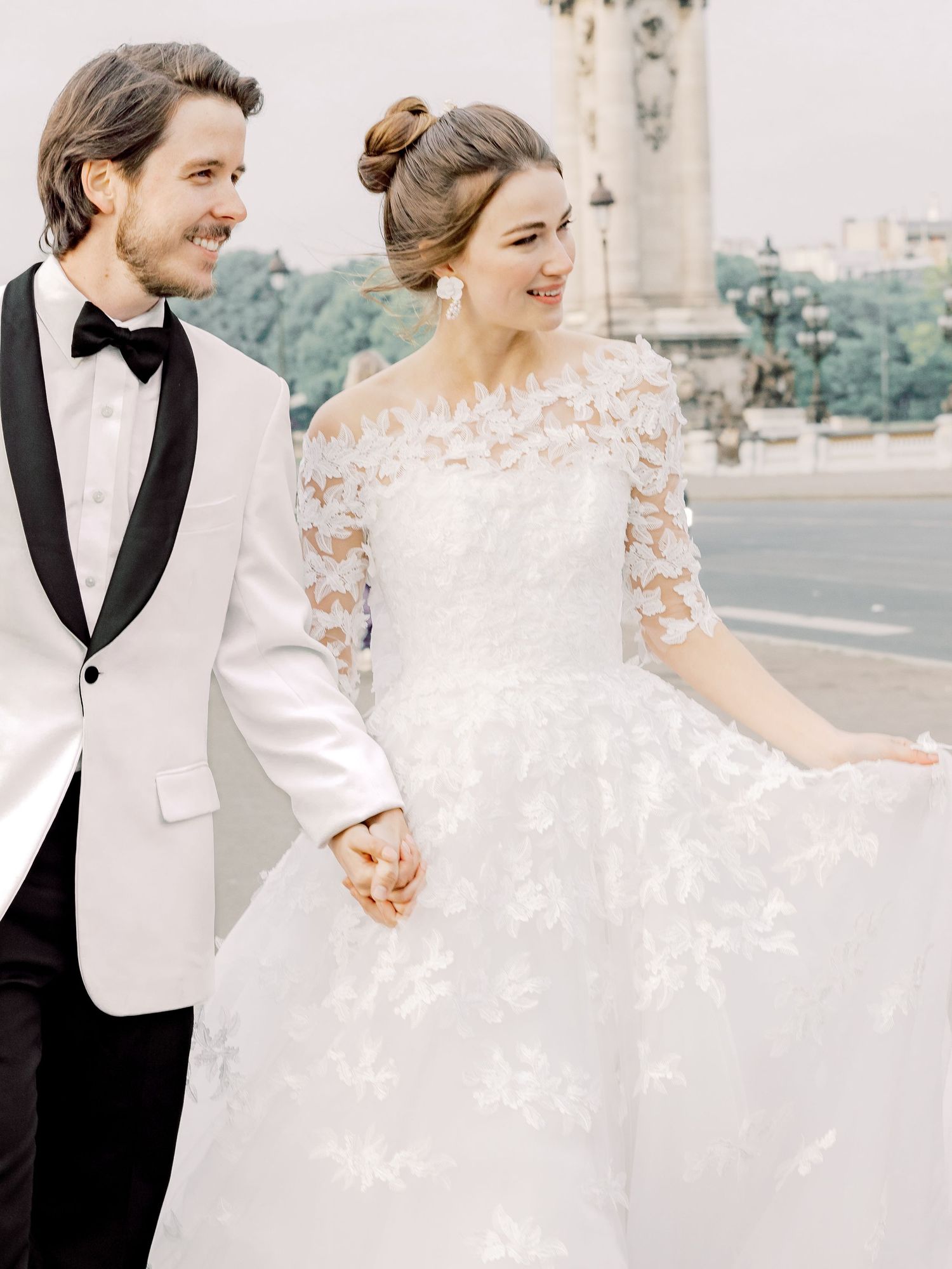 A joyful wedding couple walking together, showcasing a detailed lace gown and white dinner jacket.