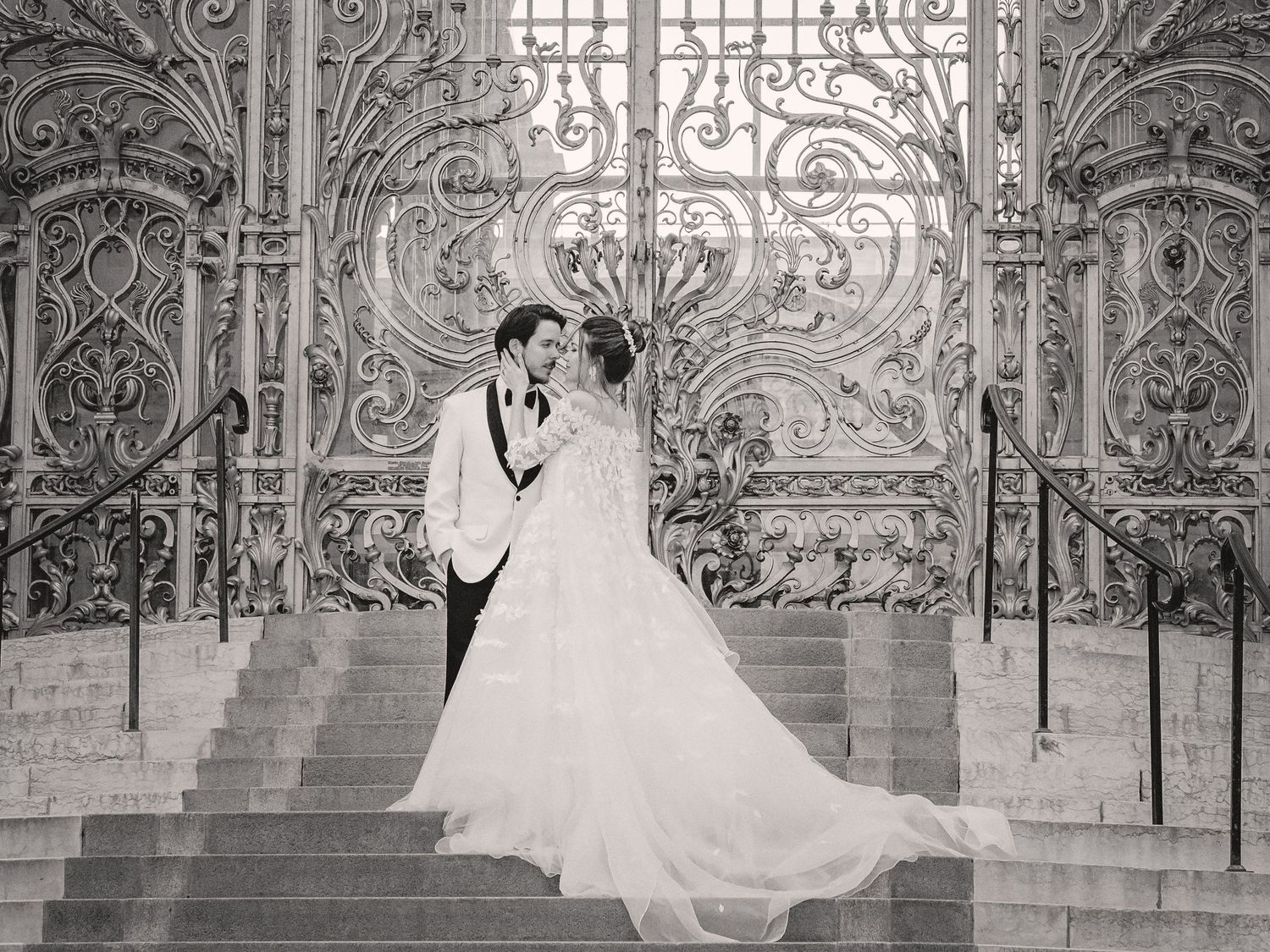 A black and white wedding photo showcasing intricate ironwork gates and architectural details.