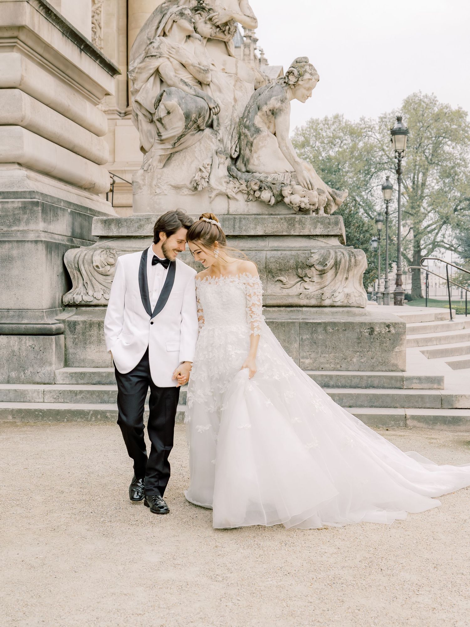 An elegant wedding couple walking beside detailed stone sculptures in formal attire.