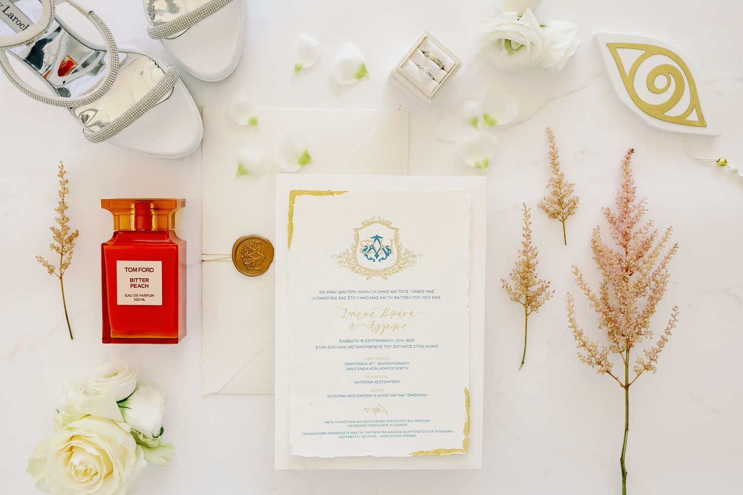 A beautiful wedding invitation, surrounded by flowers and shoes, placed on a pristine white table.