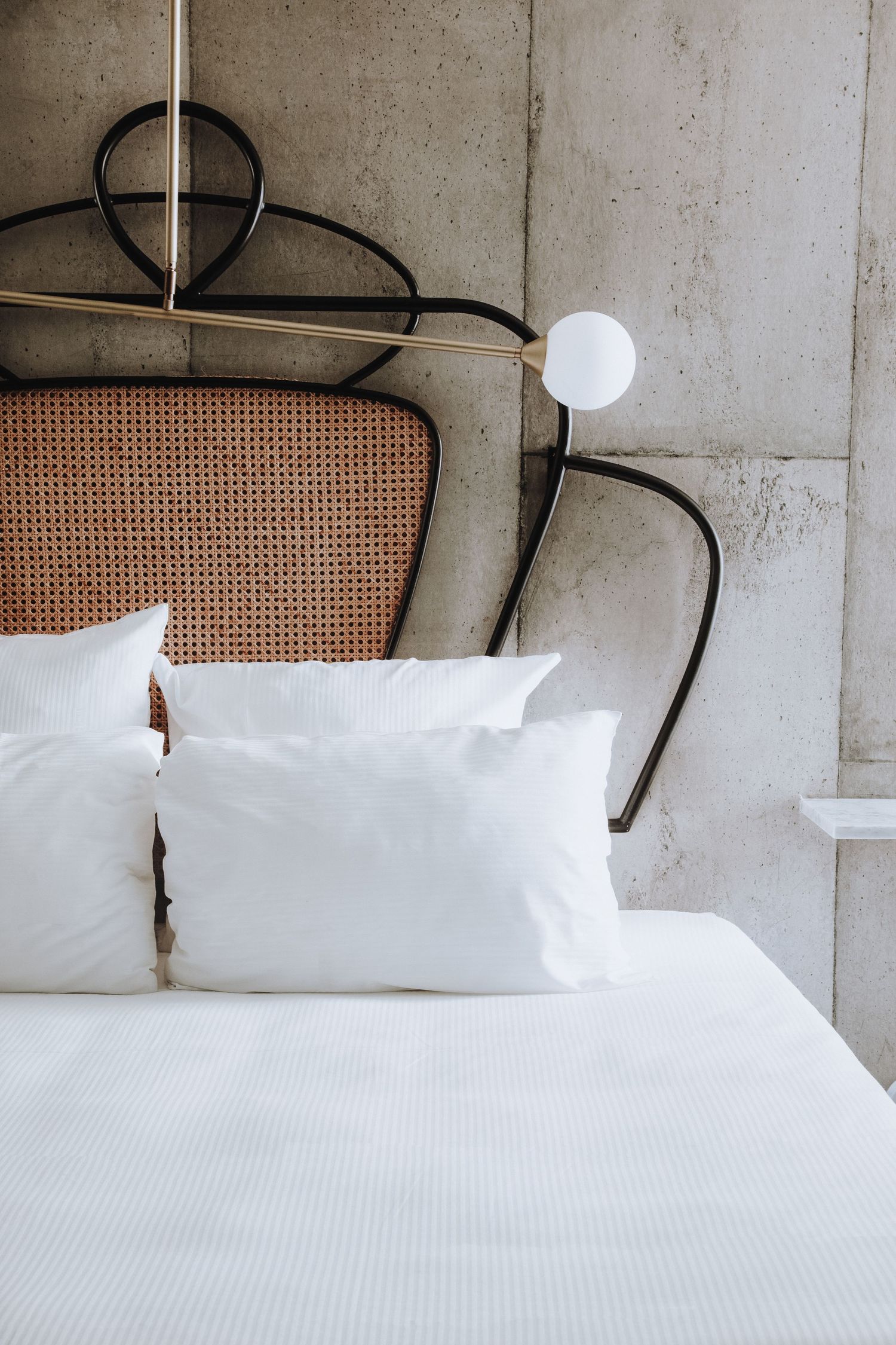 Minimalist bedroom detail with rattan headboard, white bedding, and modern wall sconce.