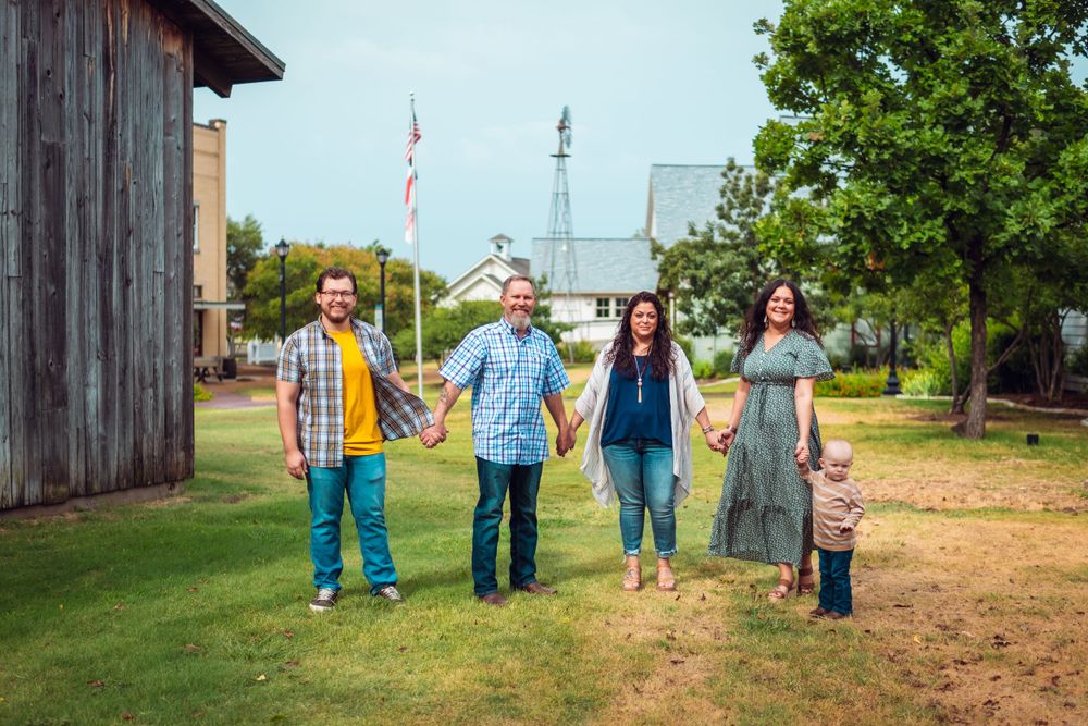 Family walking along rustic wooden buildings with trees in background.
