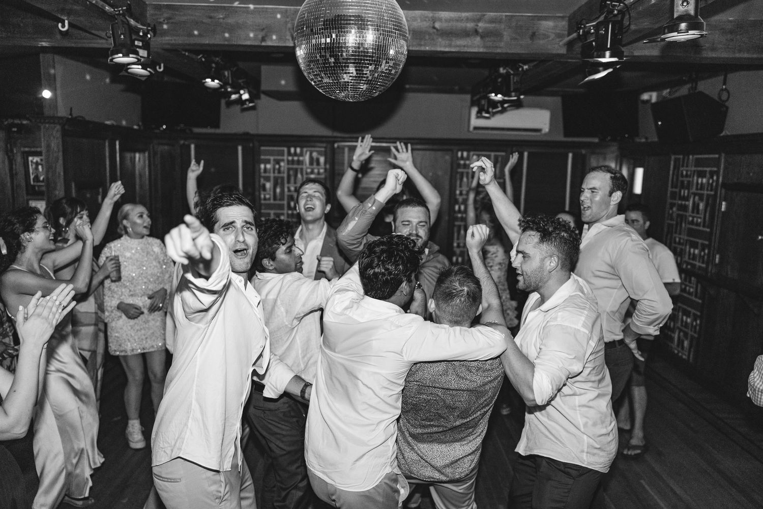 People dancing under a disco ball at a party in black and white.