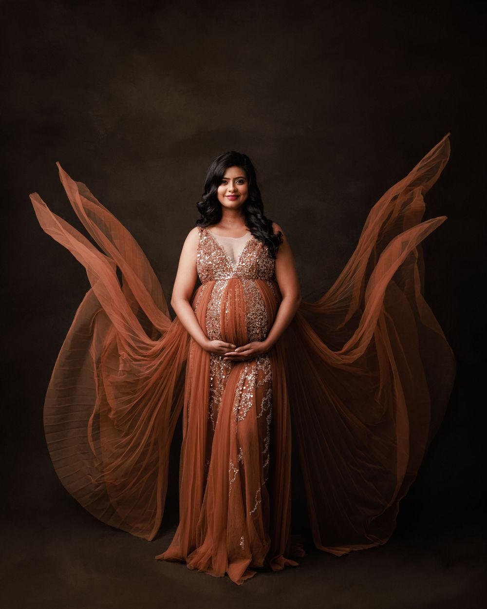 Dramatic maternity portrait in flowing copper gown with floating fabric effect.