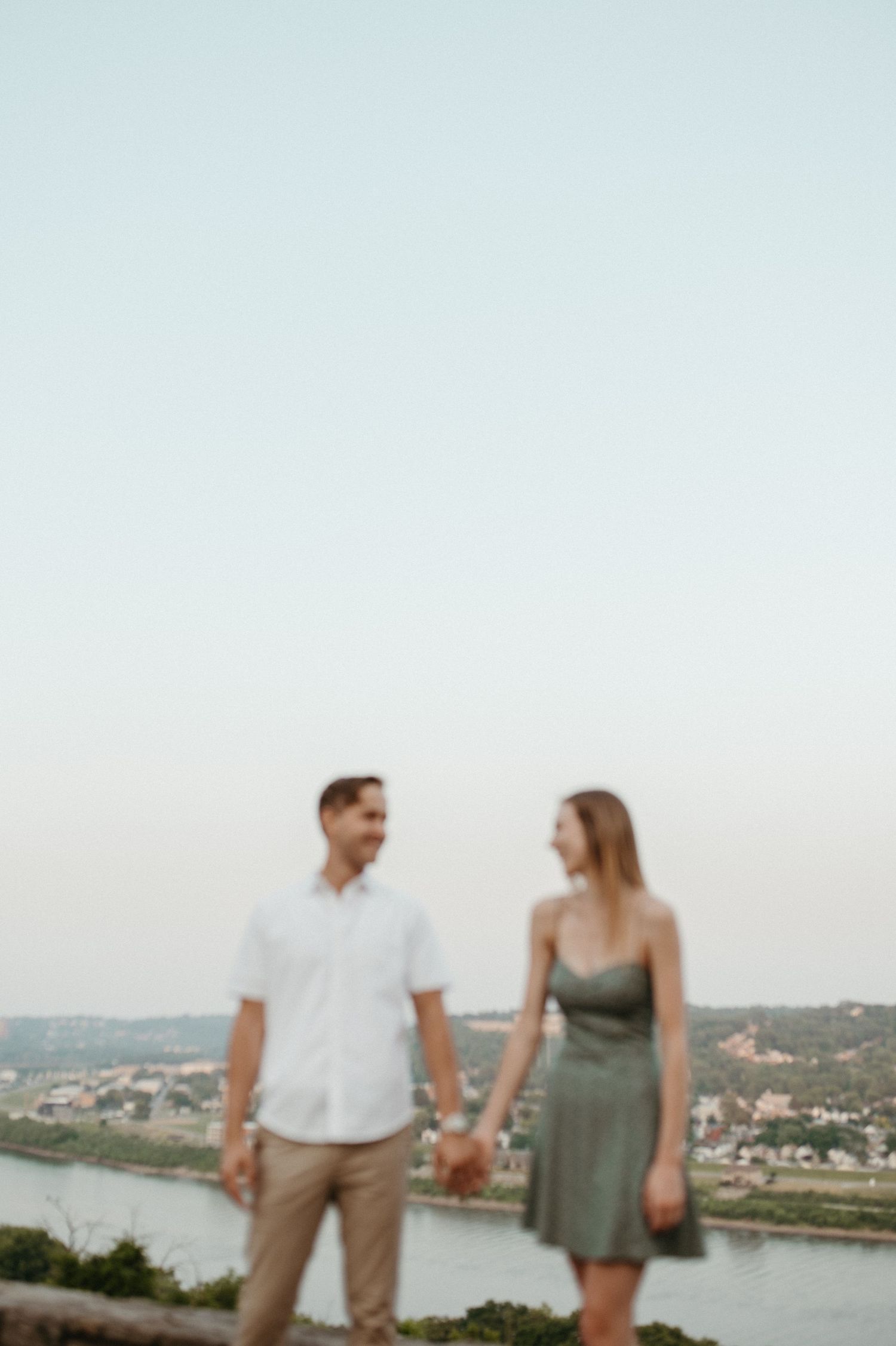 Couple stands together against scenic overlook with river view in background.