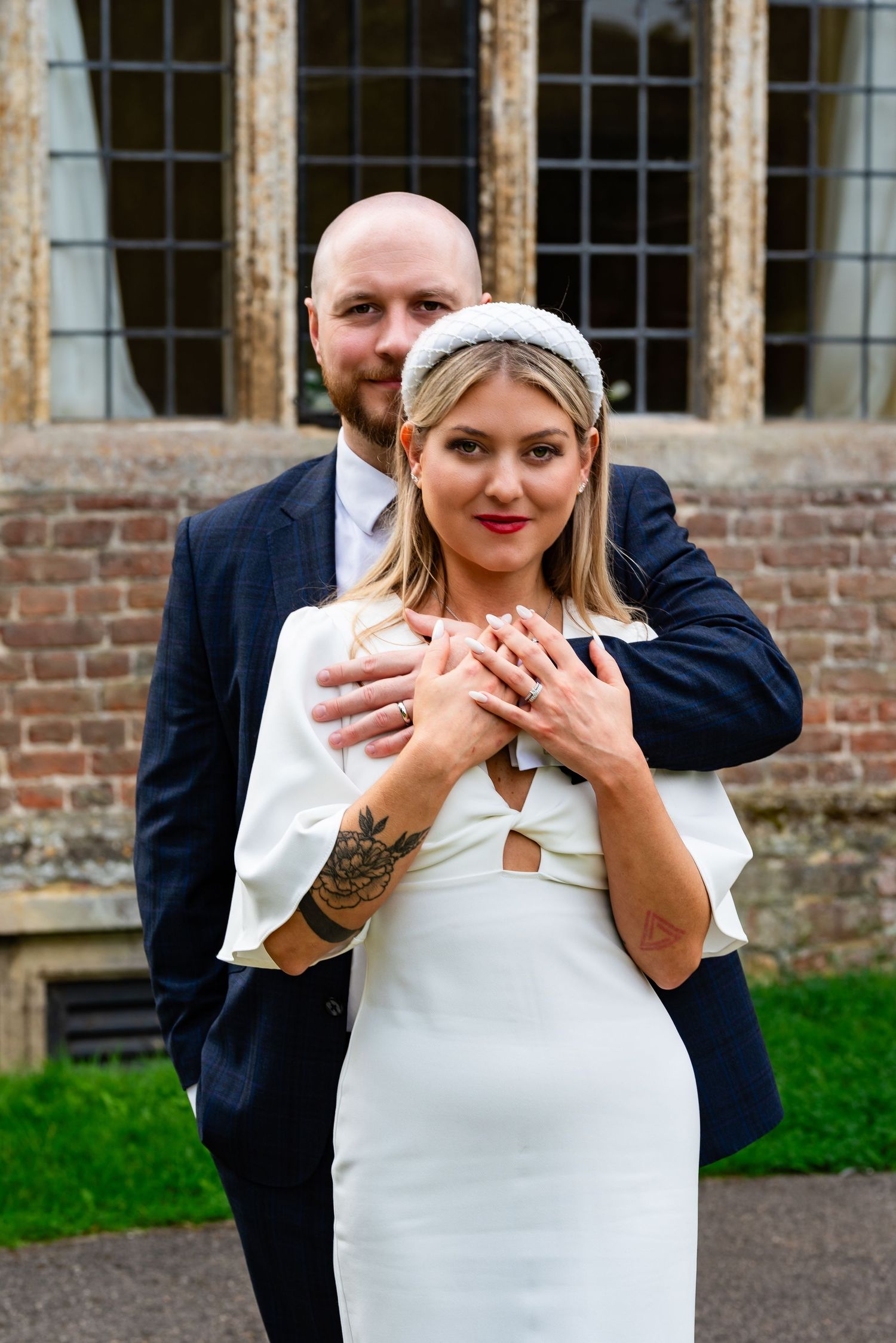 Bride in white dress and groom in navy suit pose together outside historic building.