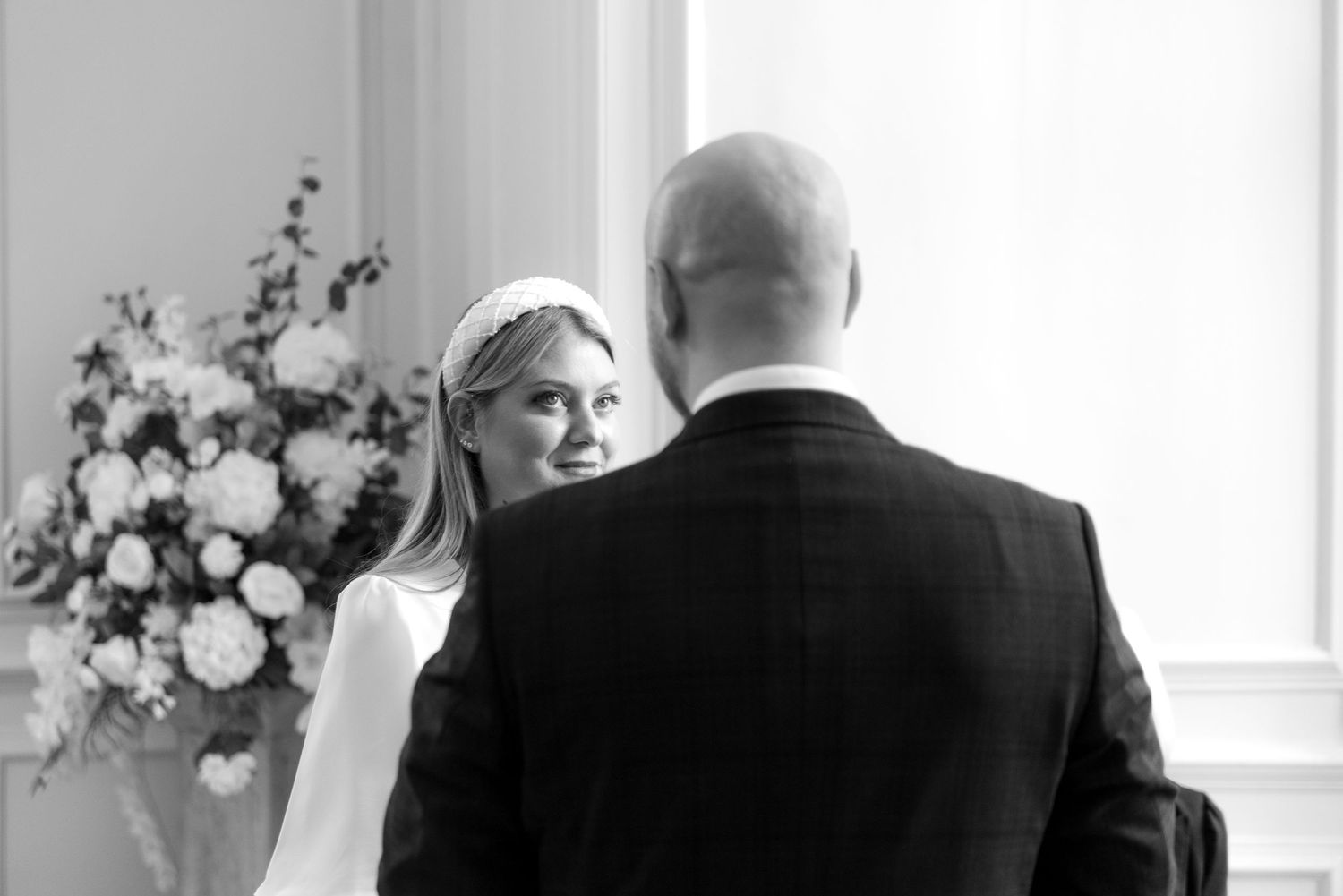 Black and white indoor wedding portrait with floral arrangement in background.