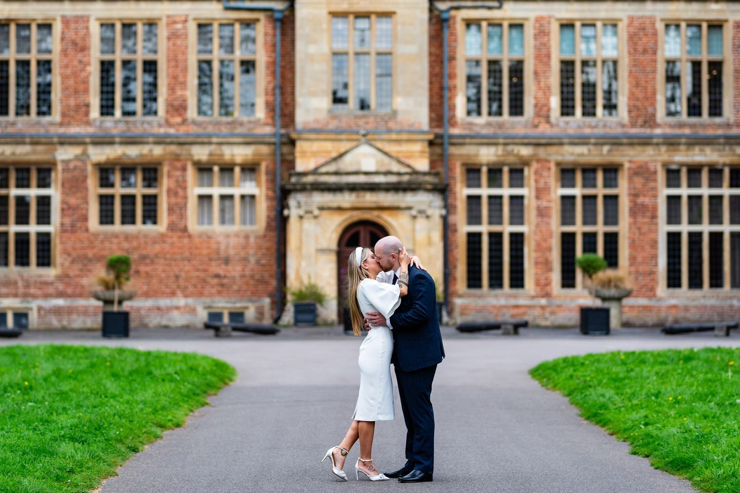 A couple shares a romantic moment on a pathway in front of a historic brick building.