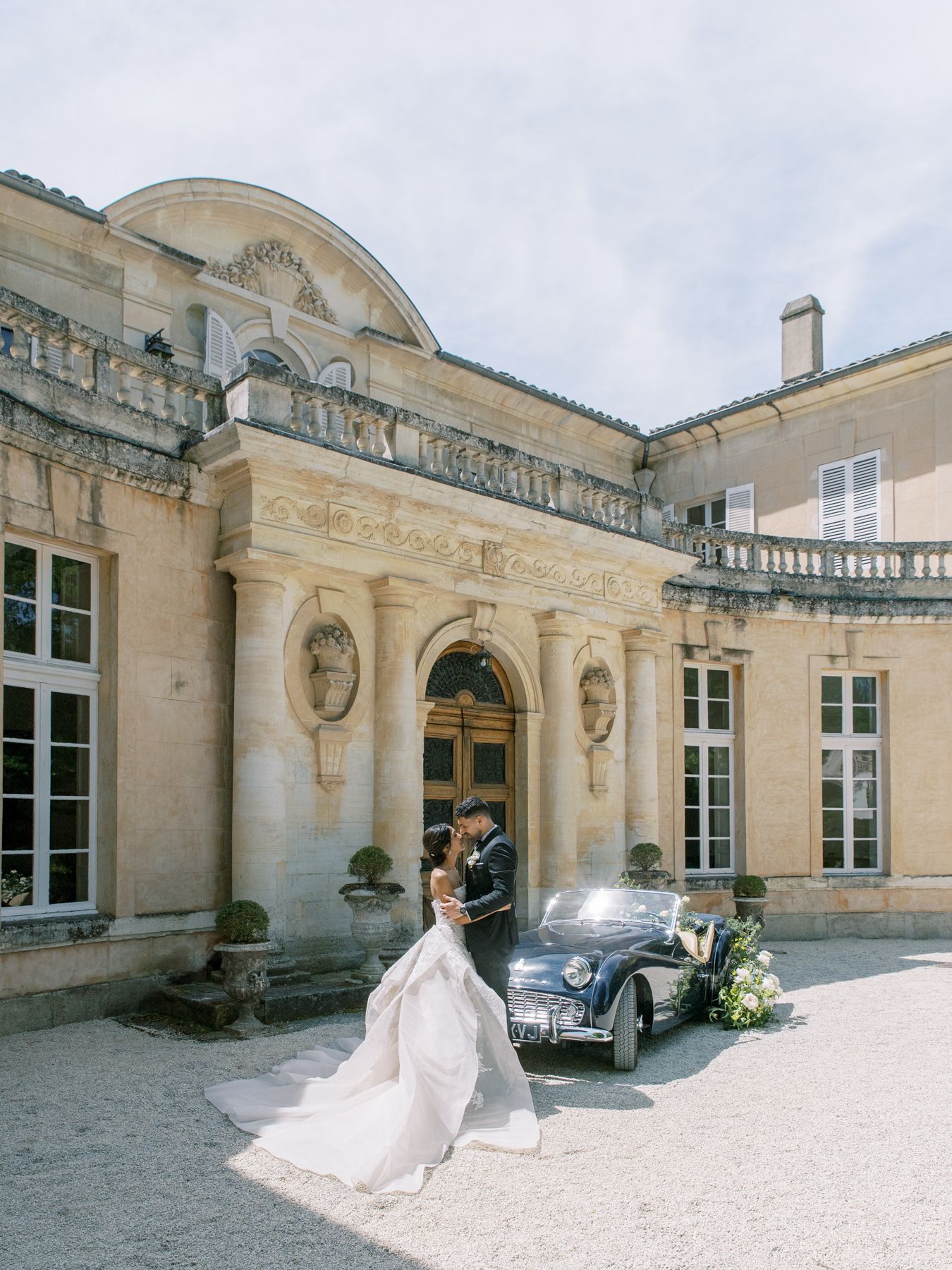 Classic vintage car parked outside elegant French chateau during wedding celebration.