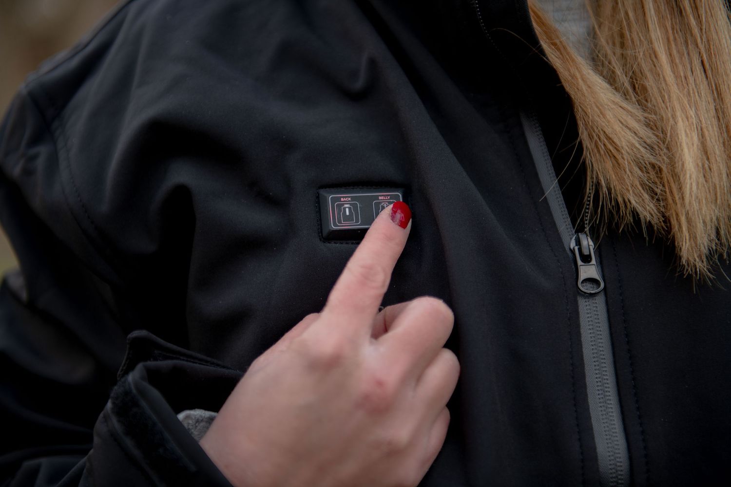 A finger pressing a button on a black waterproof jacket.