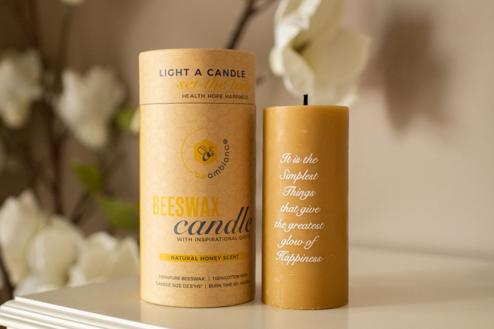 Golden beeswax candle in eco-friendly packaging with white floral decor.
