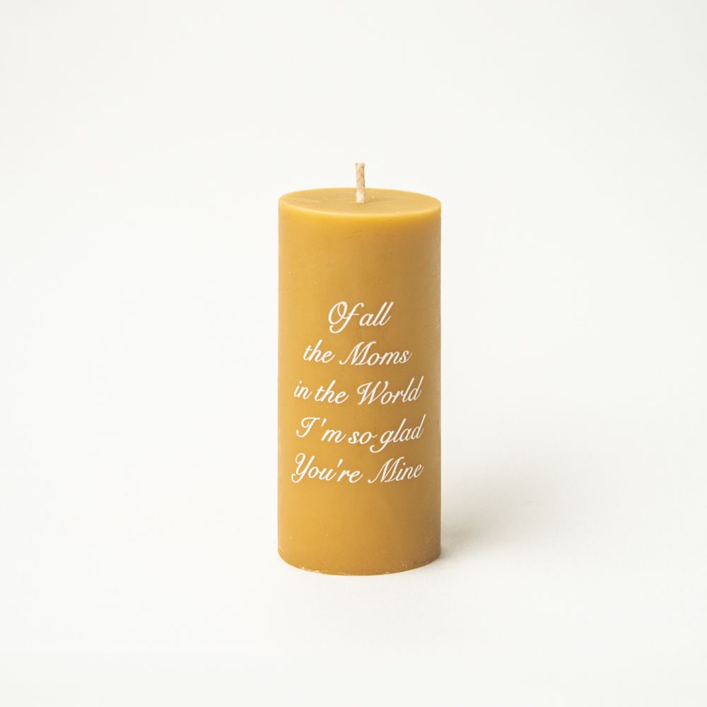 Golden pillar candle with inspirational text engraved on its surface against white background.