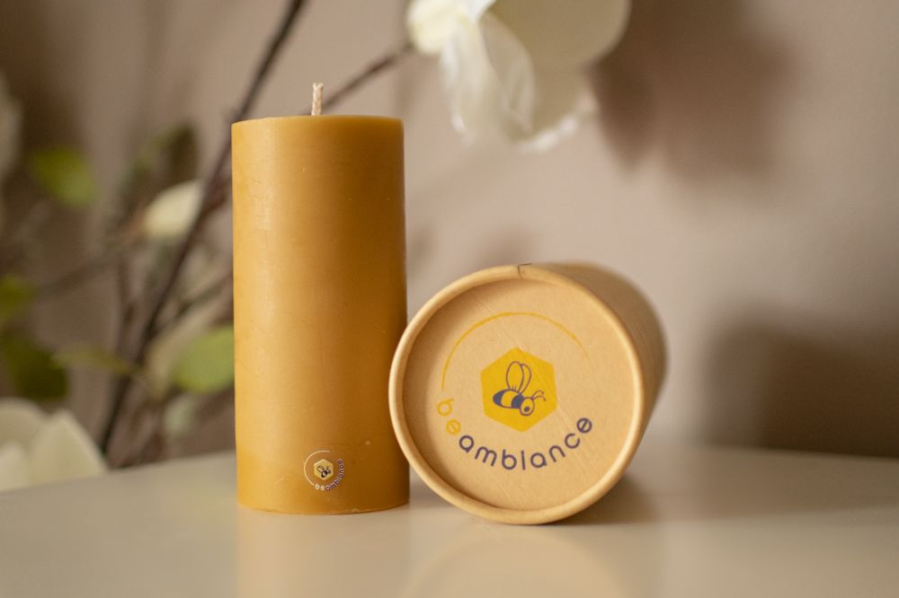 Close-up of amber-colored candle with Ambioland branded packaging on white surface.
