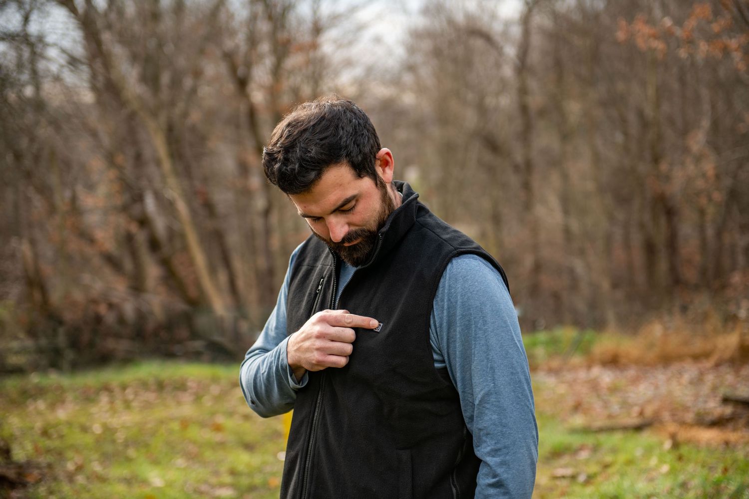 Someone adjusting their black vest while standing outdoors in a forest setting.