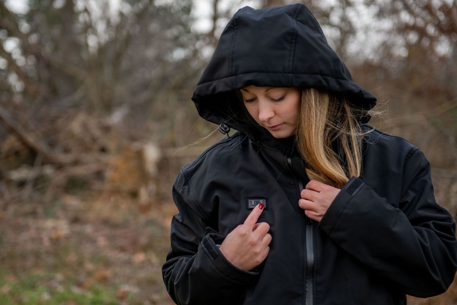 Person wearing a black hooded jacket and beanie in an outdoor wooded setting.