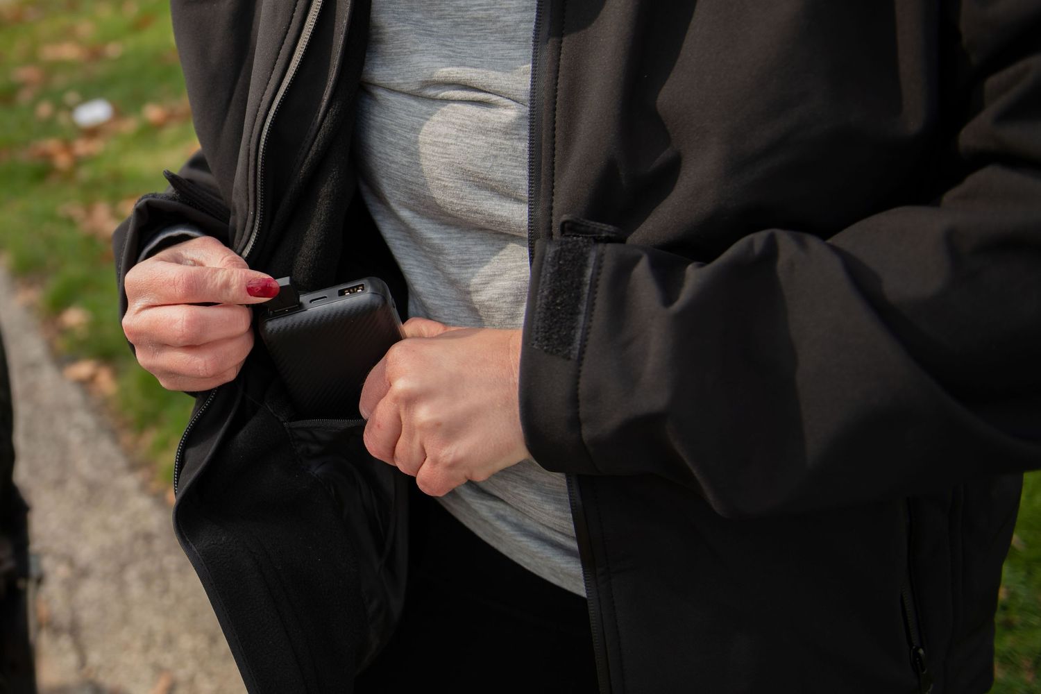 Hands adjusting a zipper on a black jacket over a grey shirt.