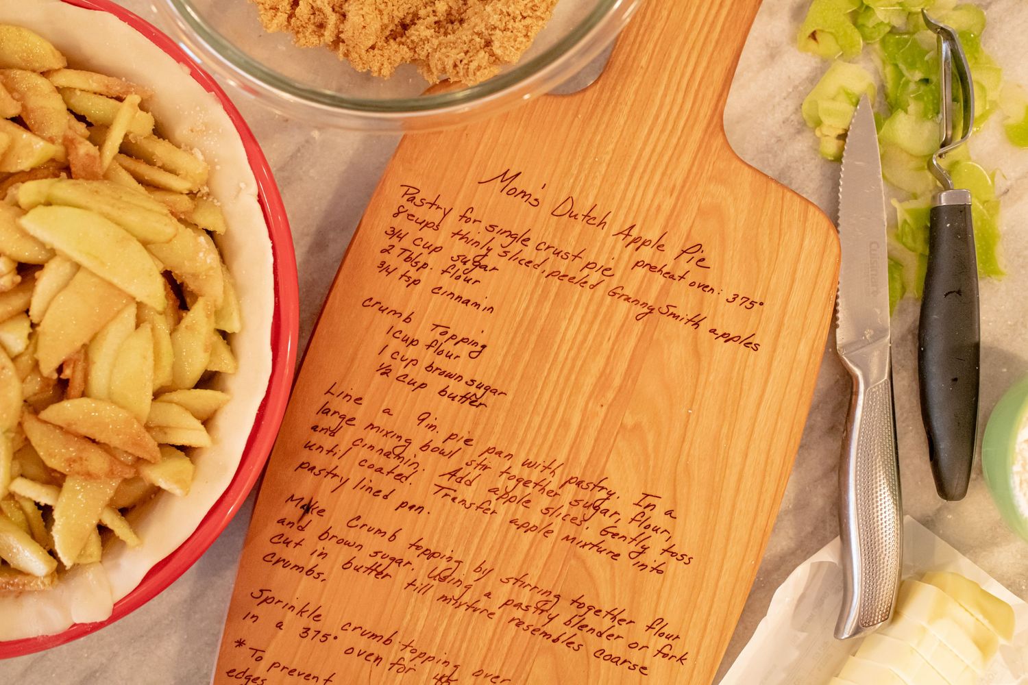 Handwritten recipe board displayed with pasta bowls and fresh vegetables on wooden surface.