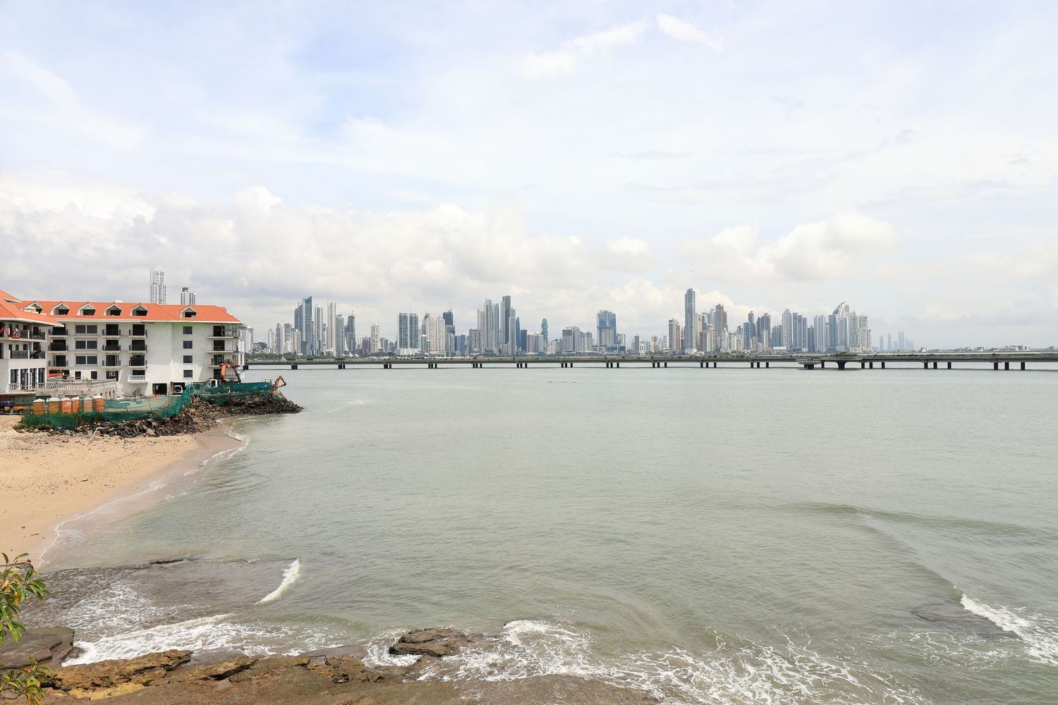Panama City skyline viewed from across the bay with waves crashing on a beach in the foreground.