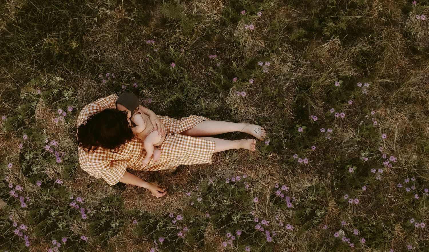 Person in flowing dress lying on ground surrounded by scattered wildflowers in aerial view.