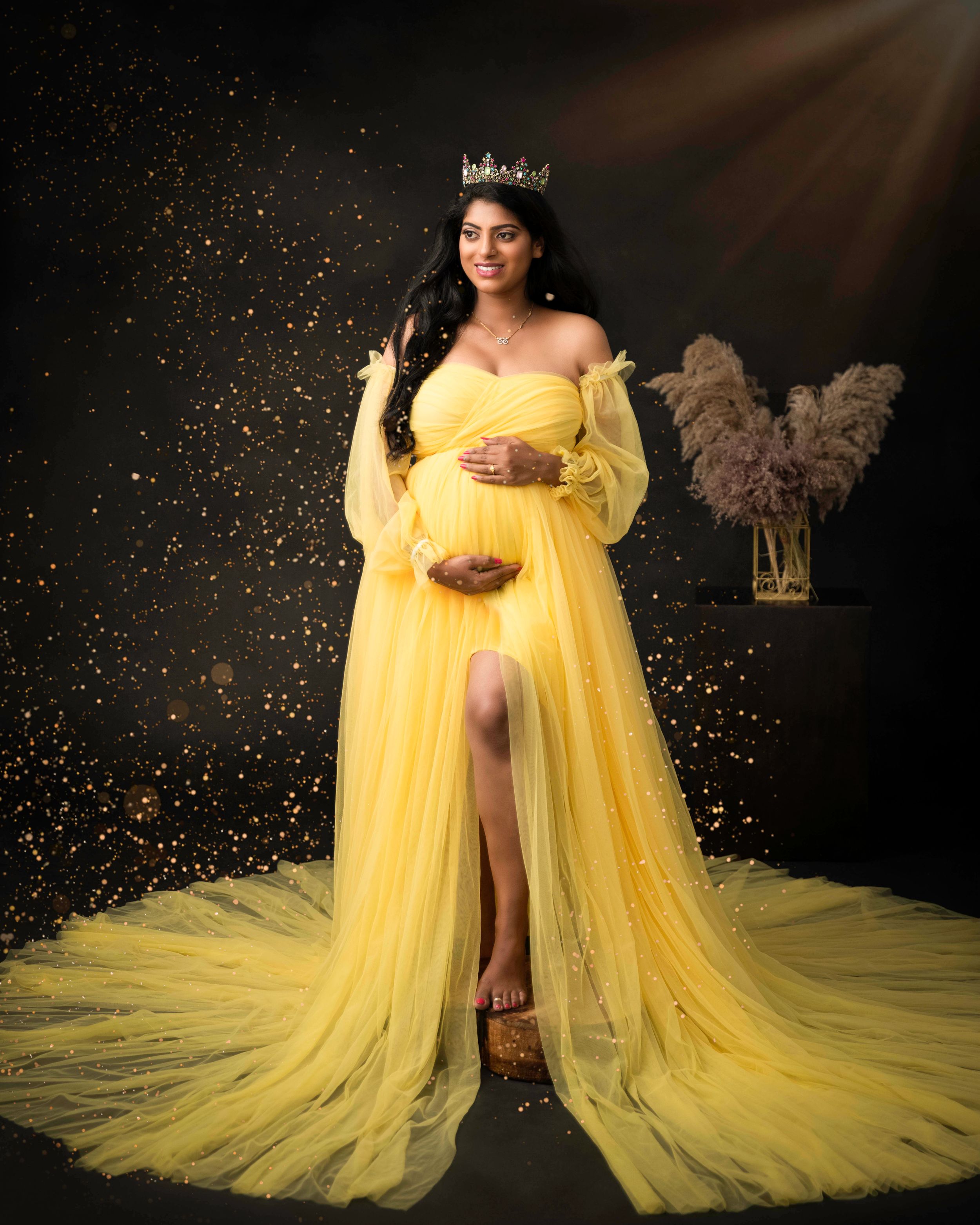 Maternity portrait in flowing yellow gown with glitter and dramatic lighting.
