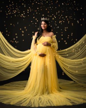Dramatic maternity photo with flowing yellow dress and sparkling backdrop.