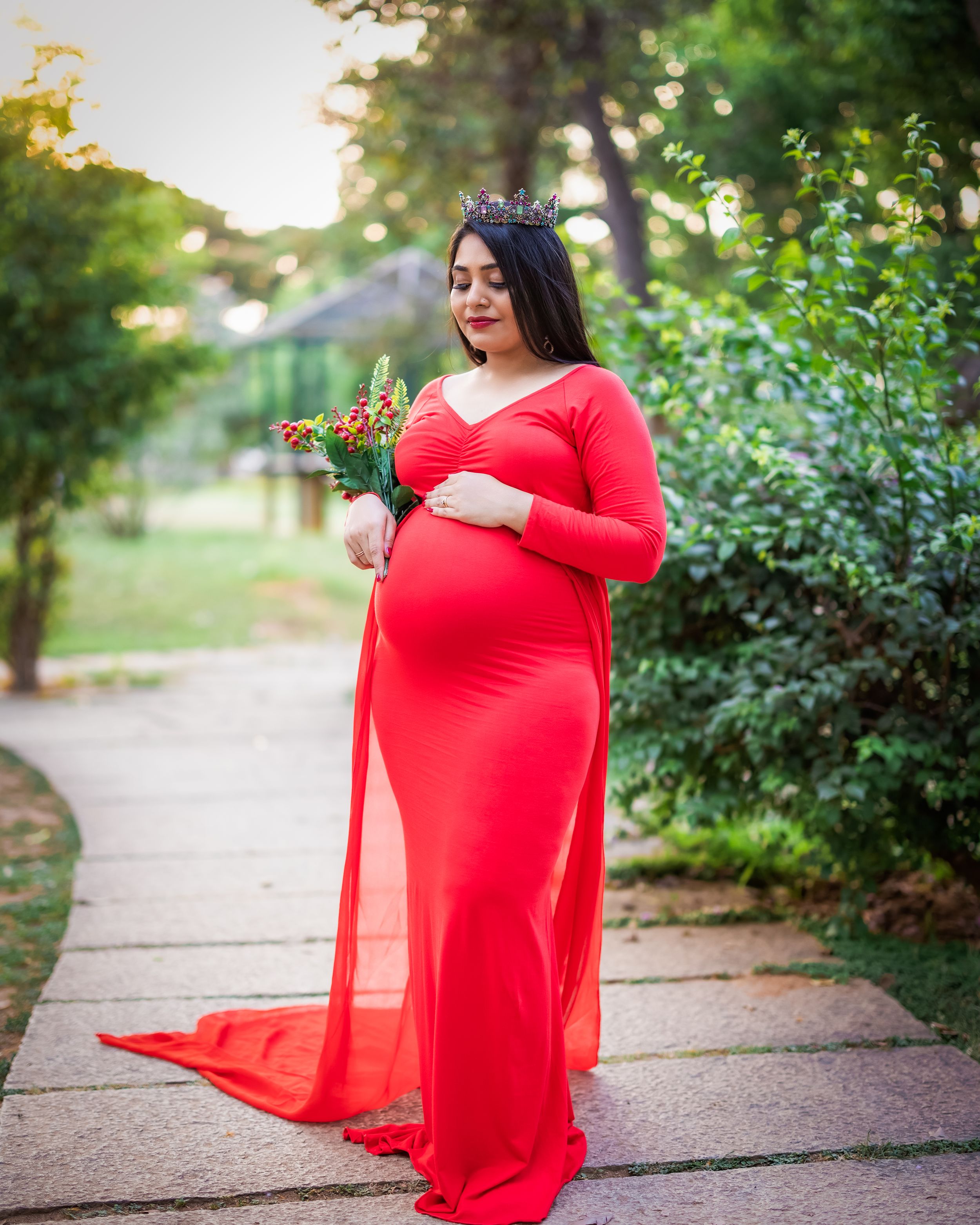 Outdoor maternity portrait in a vibrant red flowing gown surrounded by greenery.