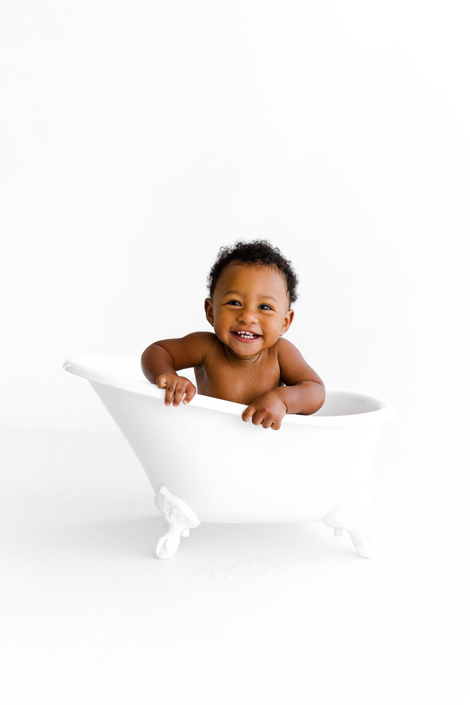 Happy baby playing in decorative white bathtub against white background.
