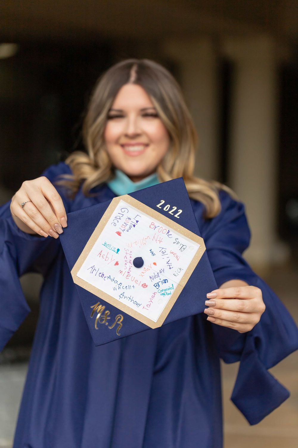 Graduate in navy cap and gown holds decorated 2022 graduation cap toward camera.