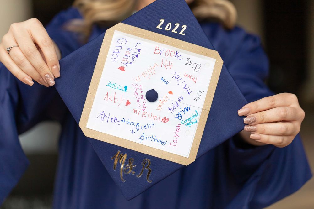 Close-up of decorated 2022 graduation cap with colorful handwritten names and messages.