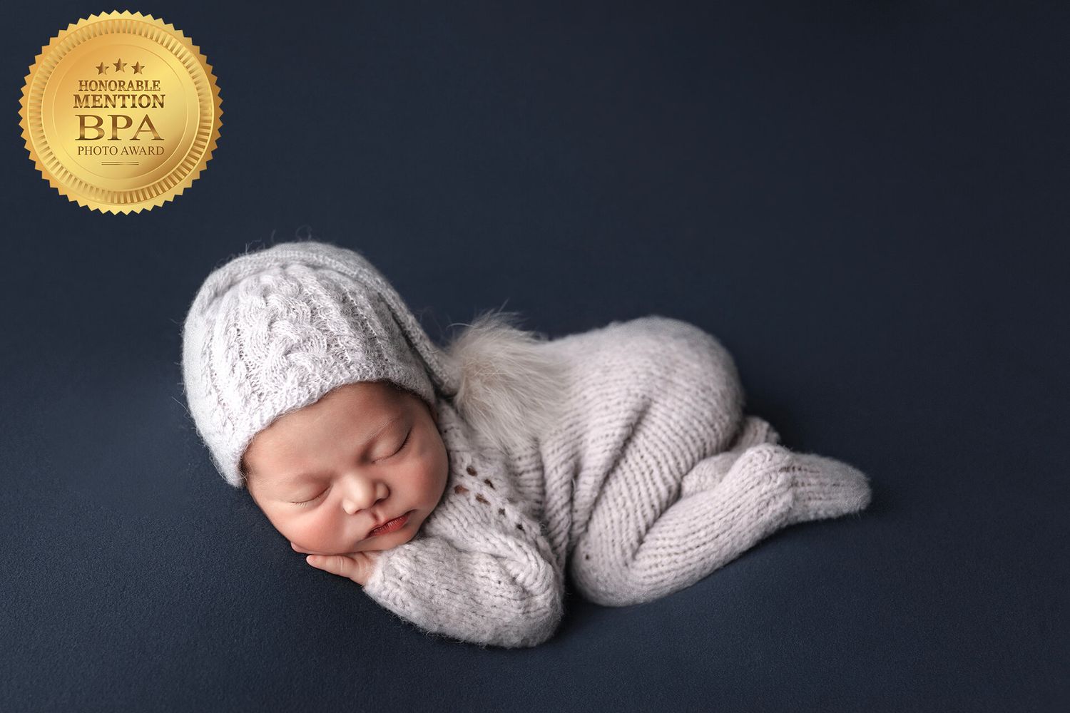 A sleeping newborn wrapped in soft gray knit wear against a dark studio backdrop.