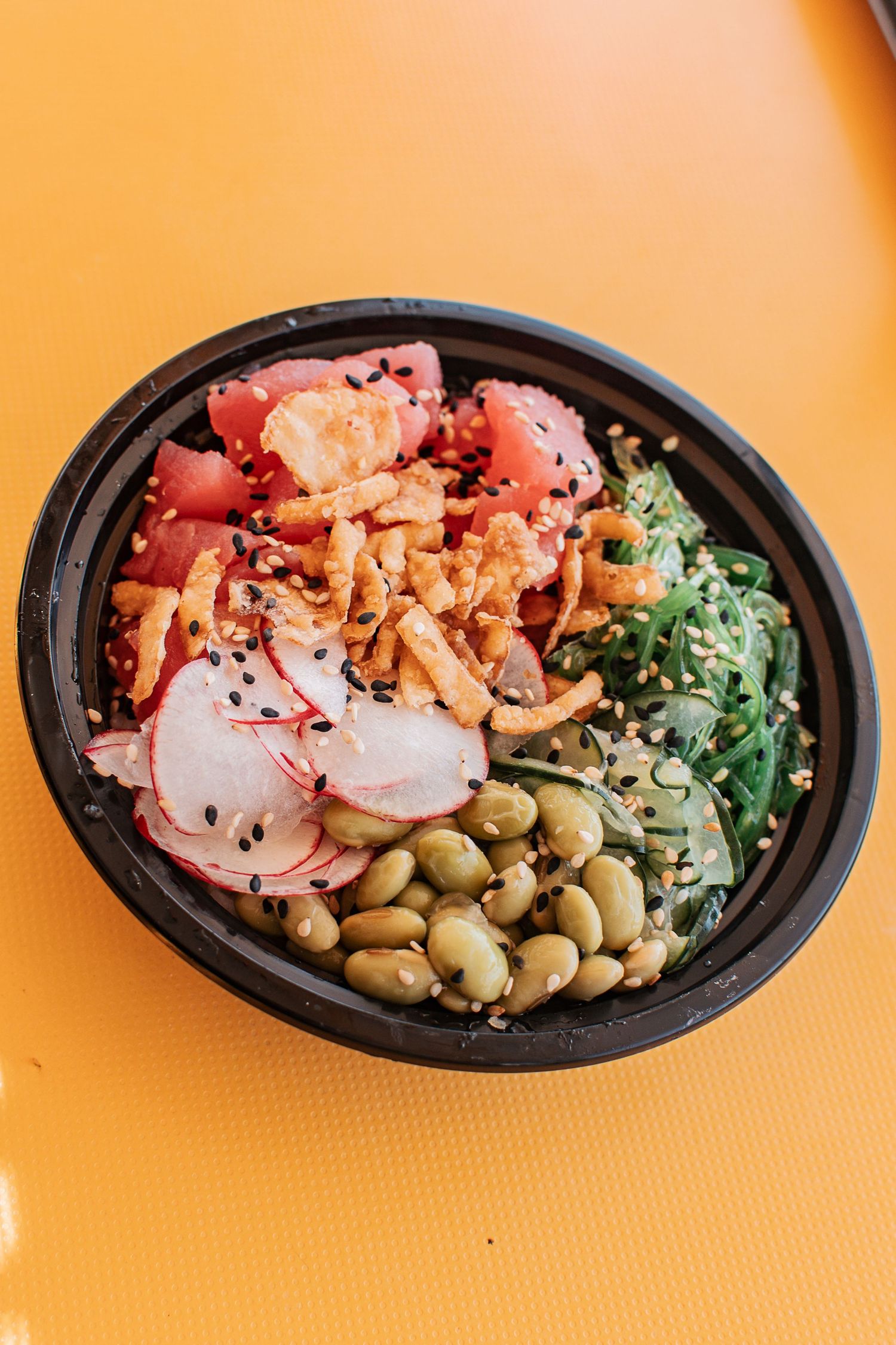 Fresh poke bowl with tuna, radishes, edamame and seaweed on orange background.