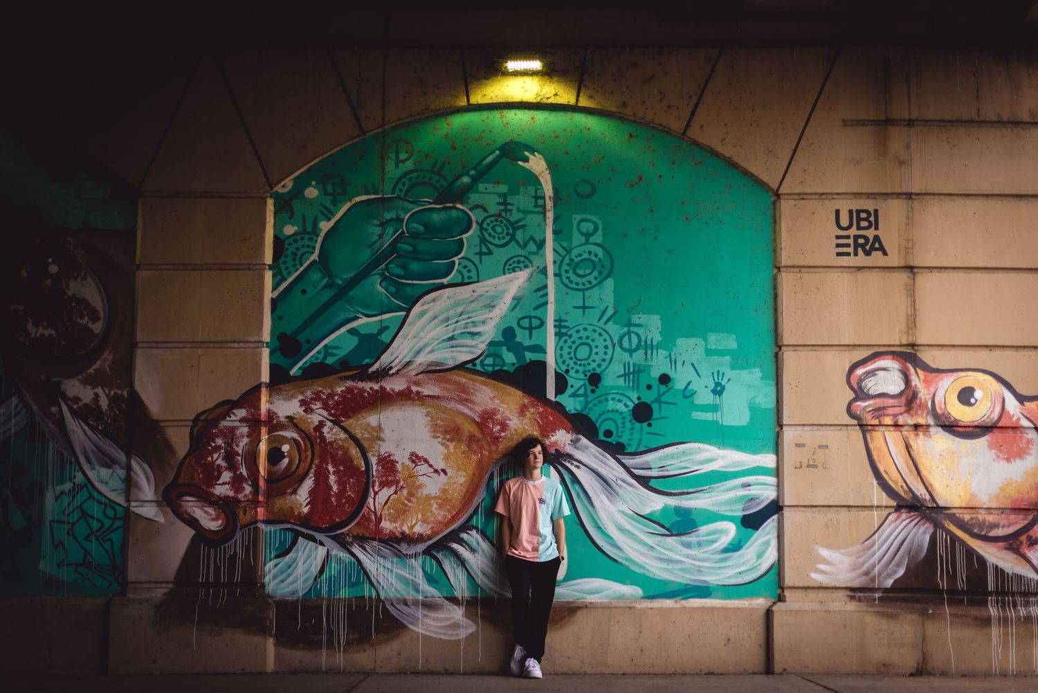 Person poses in front of vibrant green underwater-themed street art mural at night.