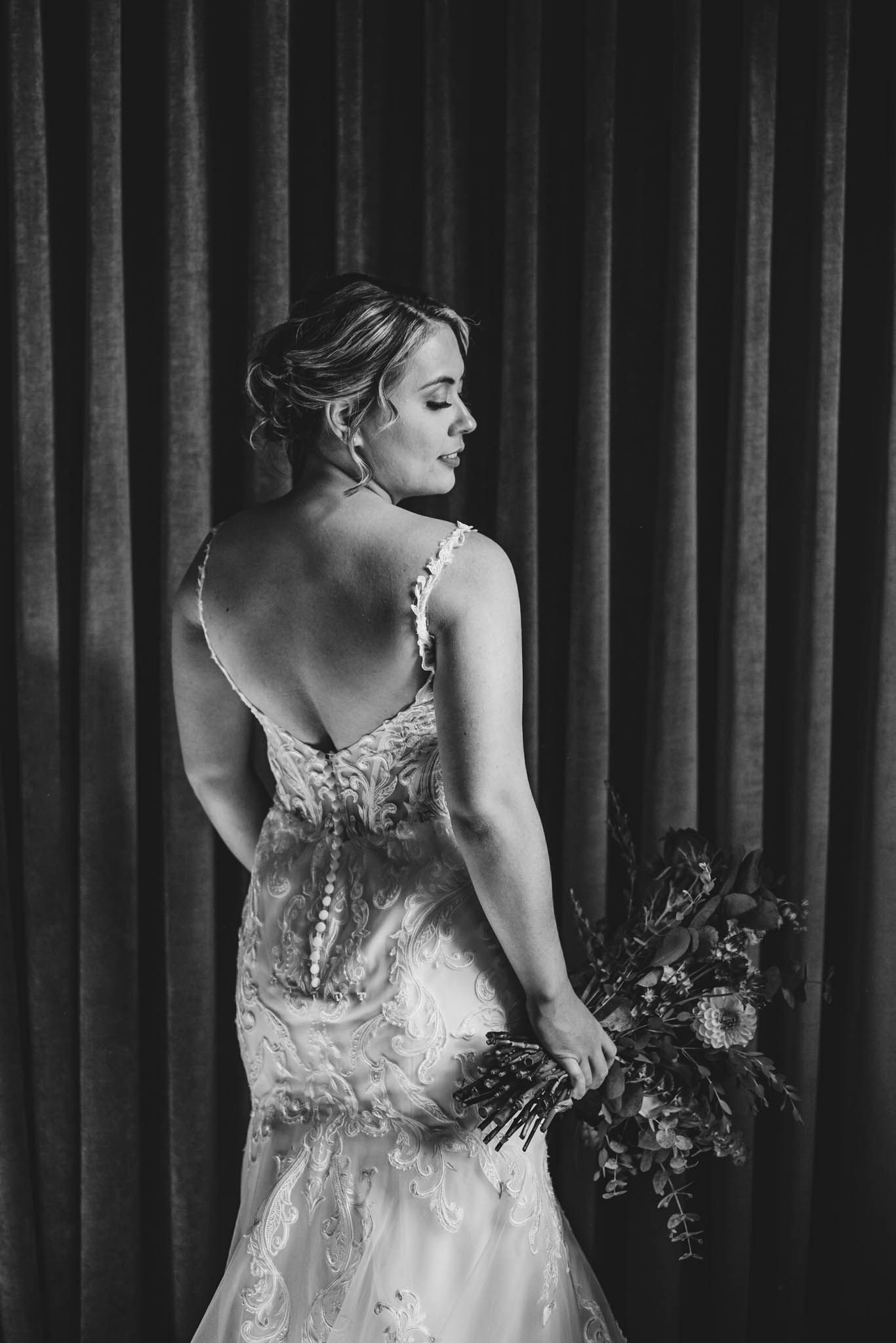 Elegant lace wedding dress details shown against dark curtain backdrop.