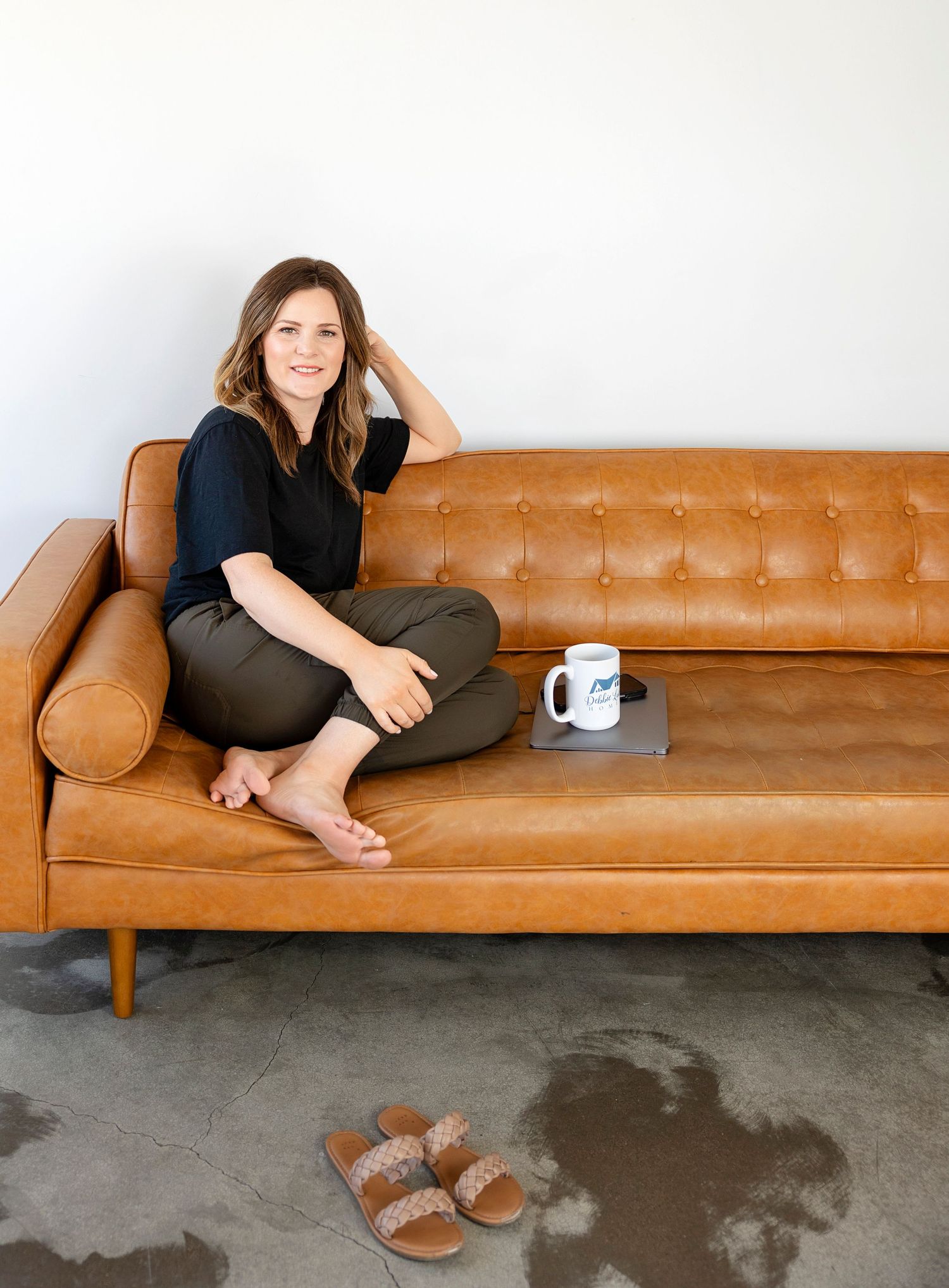 Person relaxing on tan leather sofa with laptop and coffee mug nearby.