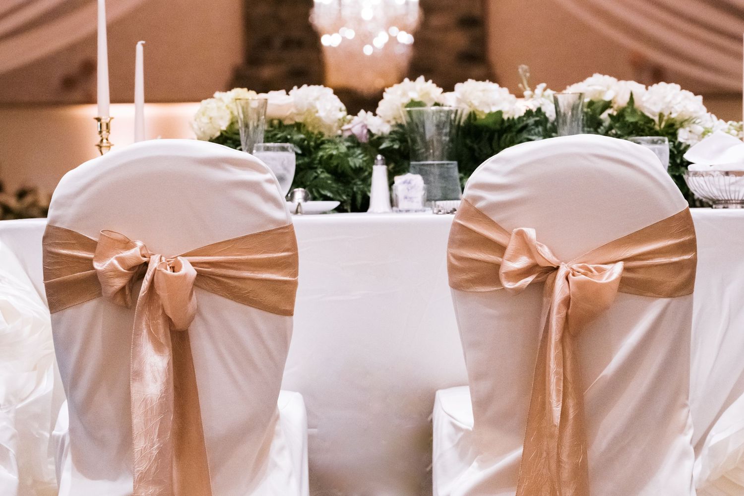 Elegant wedding reception chairs with champagne-colored sashes and white covers.