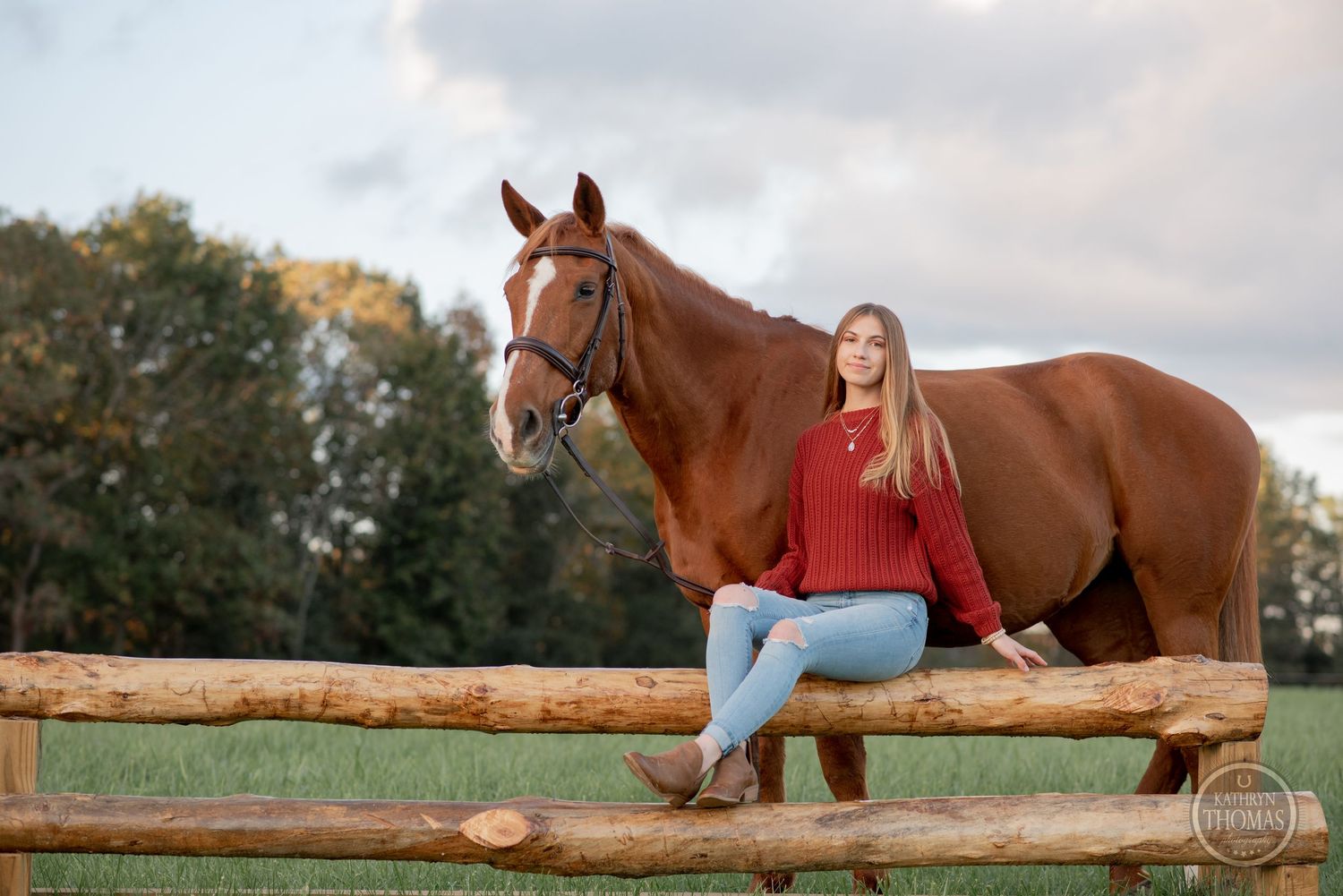 Horse and rider sitting on wooden fence during cloudy autumn evening.