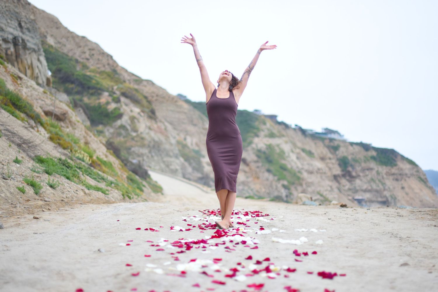 Woman in purple dress celebrates on beach path with rose petals scattered at her feet.