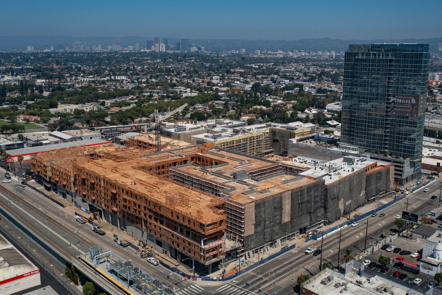 Overhead drone shot of a massive mixed-use commercial development project underway, showing extensive wood framing and site infrastructure.