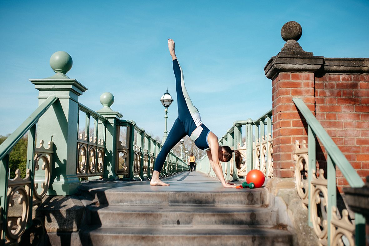 Dancers performing acrobatic moves on historic stone bridge steps against bright blue sky.