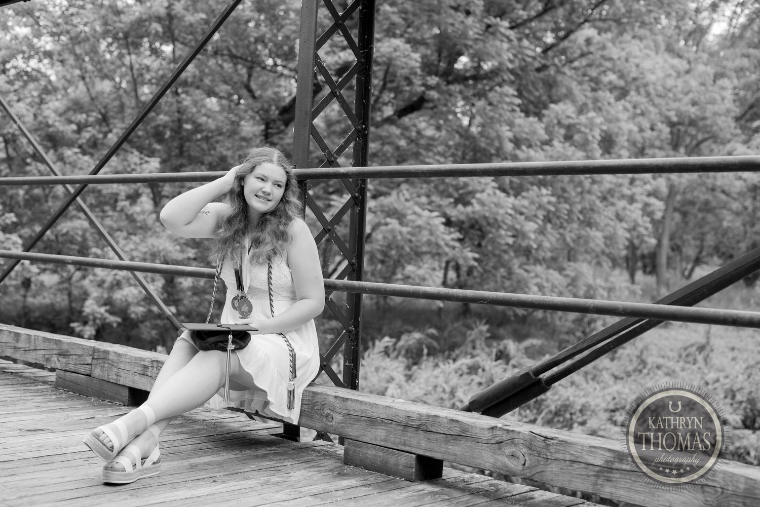 Black and white graduation portrait on rustic bridge with natural lighting.