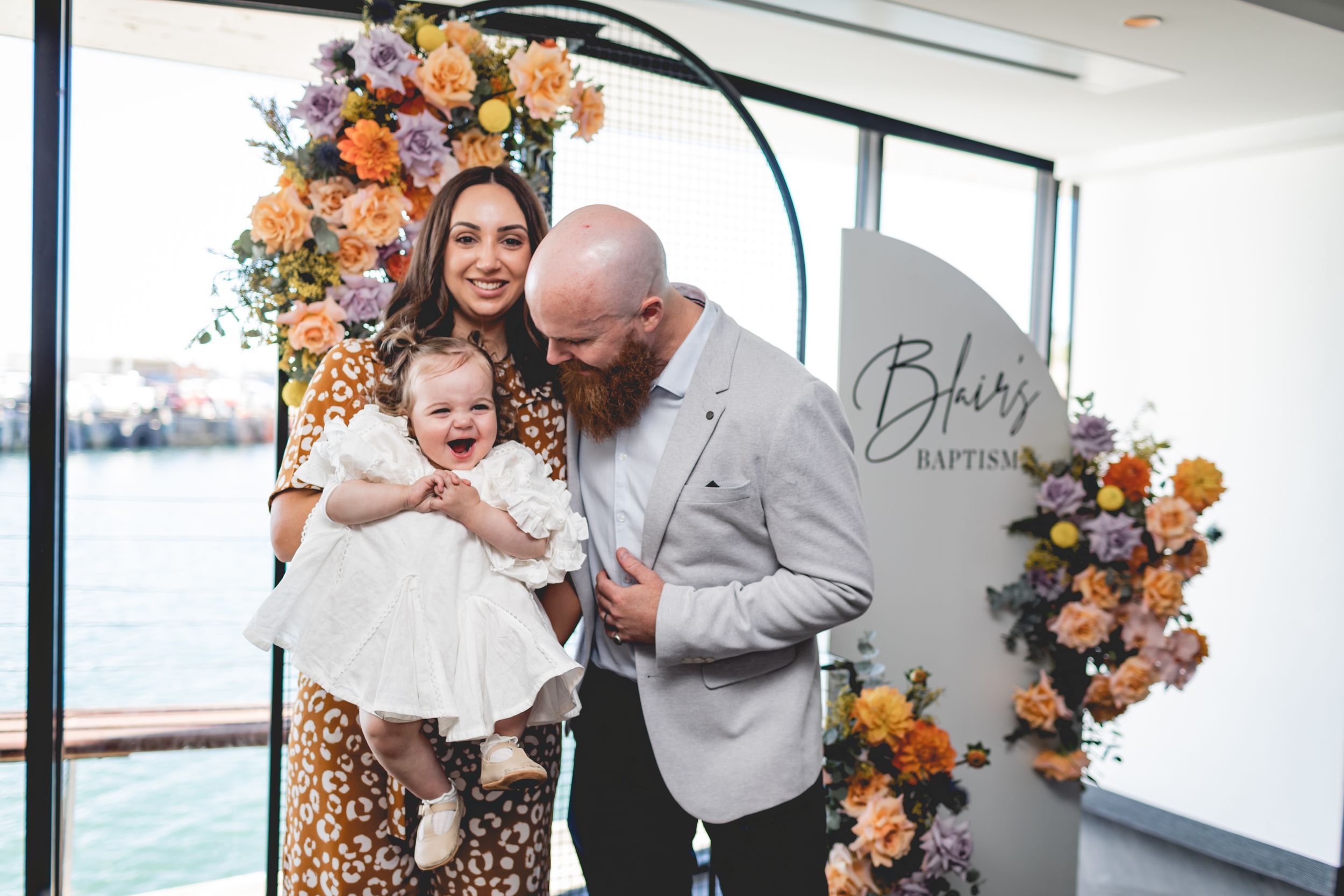 Family moment during baptism celebration with peach and orange floral arch.