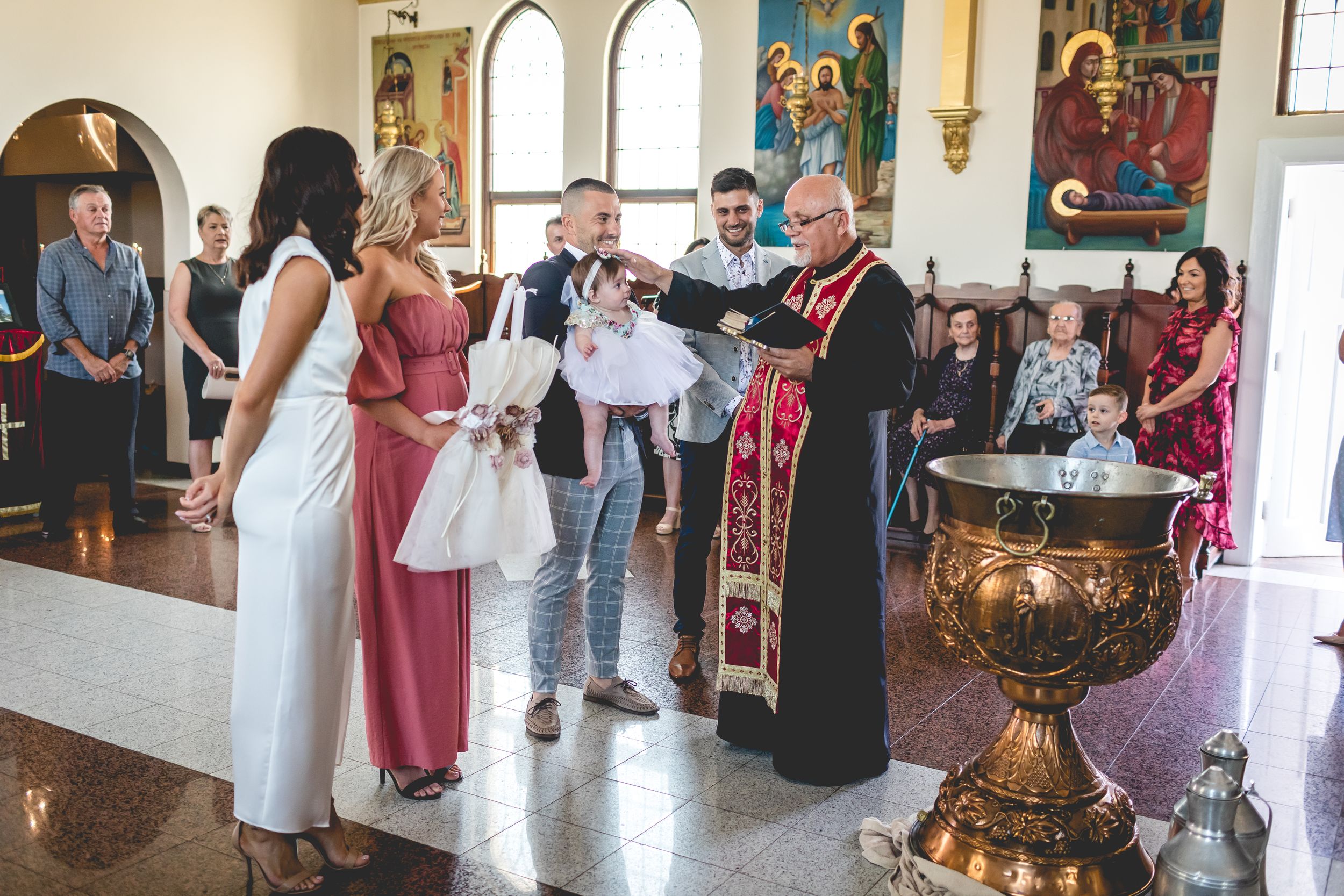 Orthodox Christian baptism ceremony taking place inside a church with religious icons and decorative elements.
