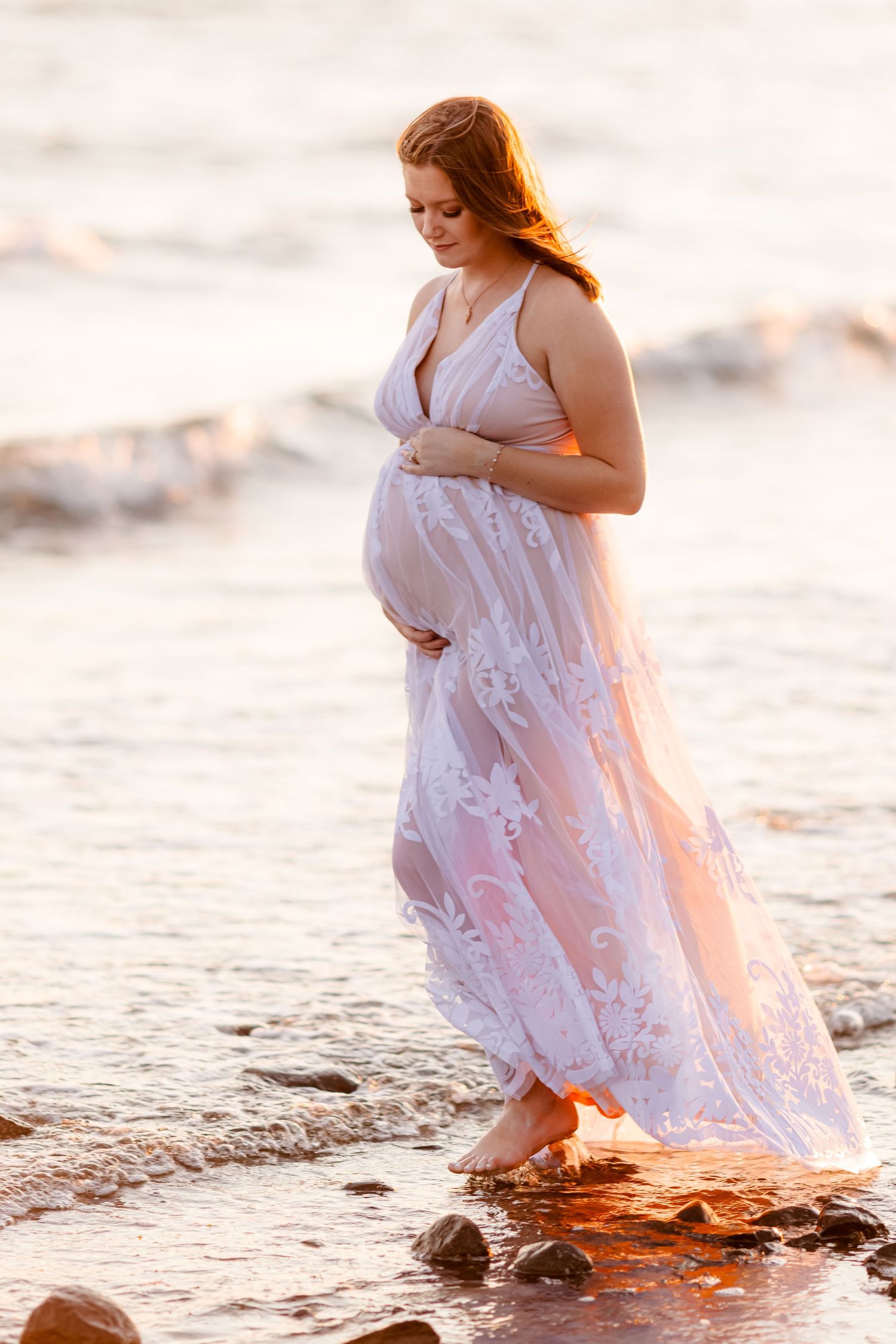 Person in flowing white dress walking through shallow water at sunset.