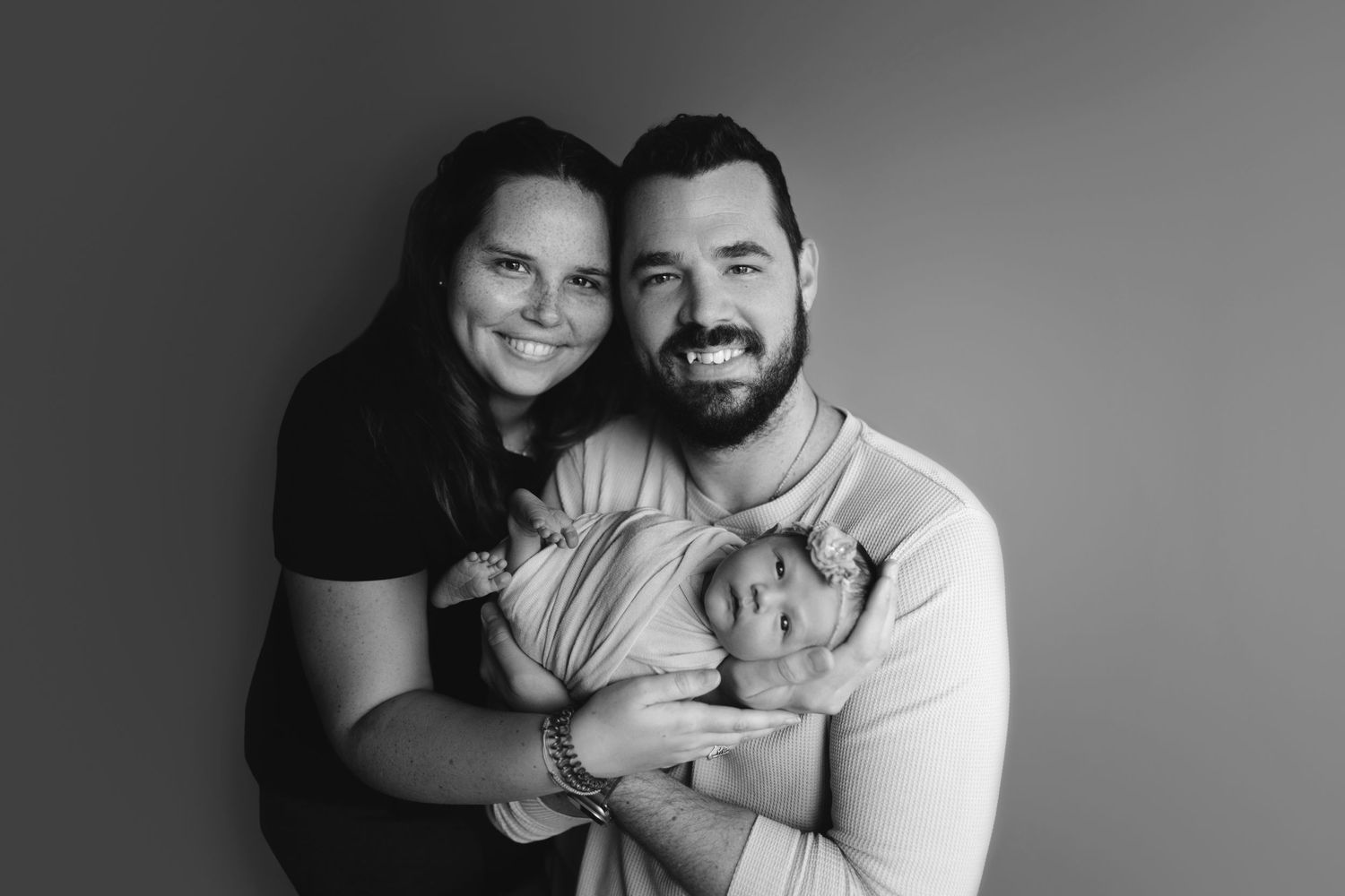Black and white portrait of family in casual attire against simple background.