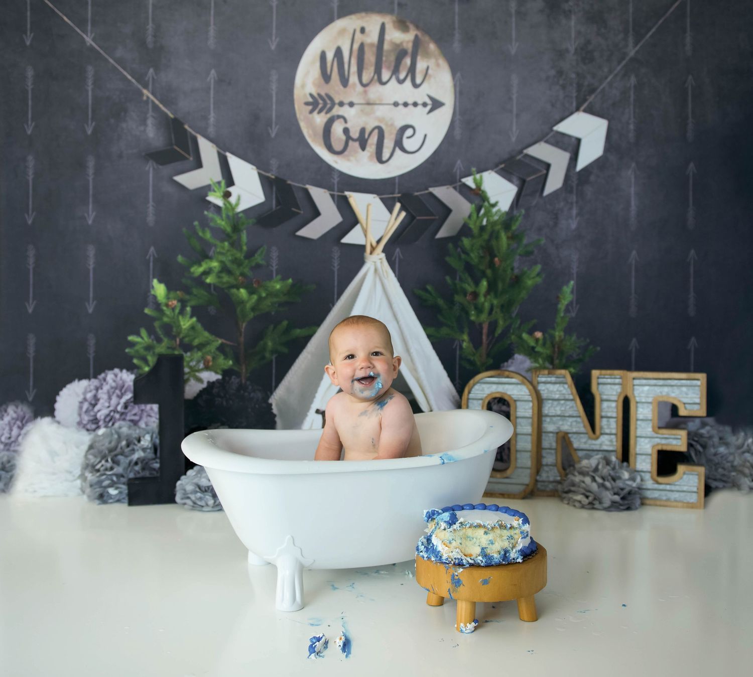 smiling one year old boy with icing on face in a bath tub