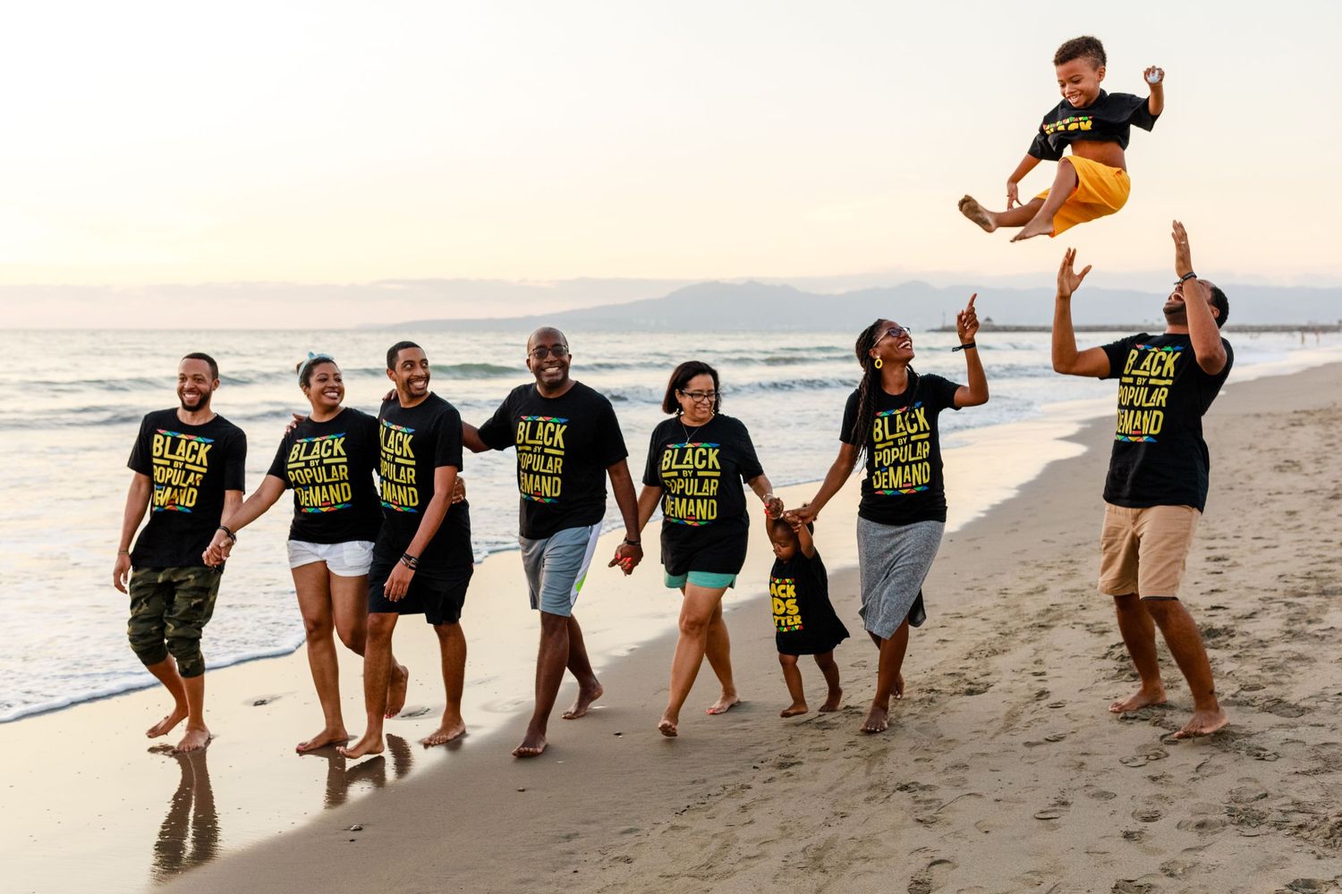 Group in matching t-shirts playfully jumping and posing together on a sunset beach.