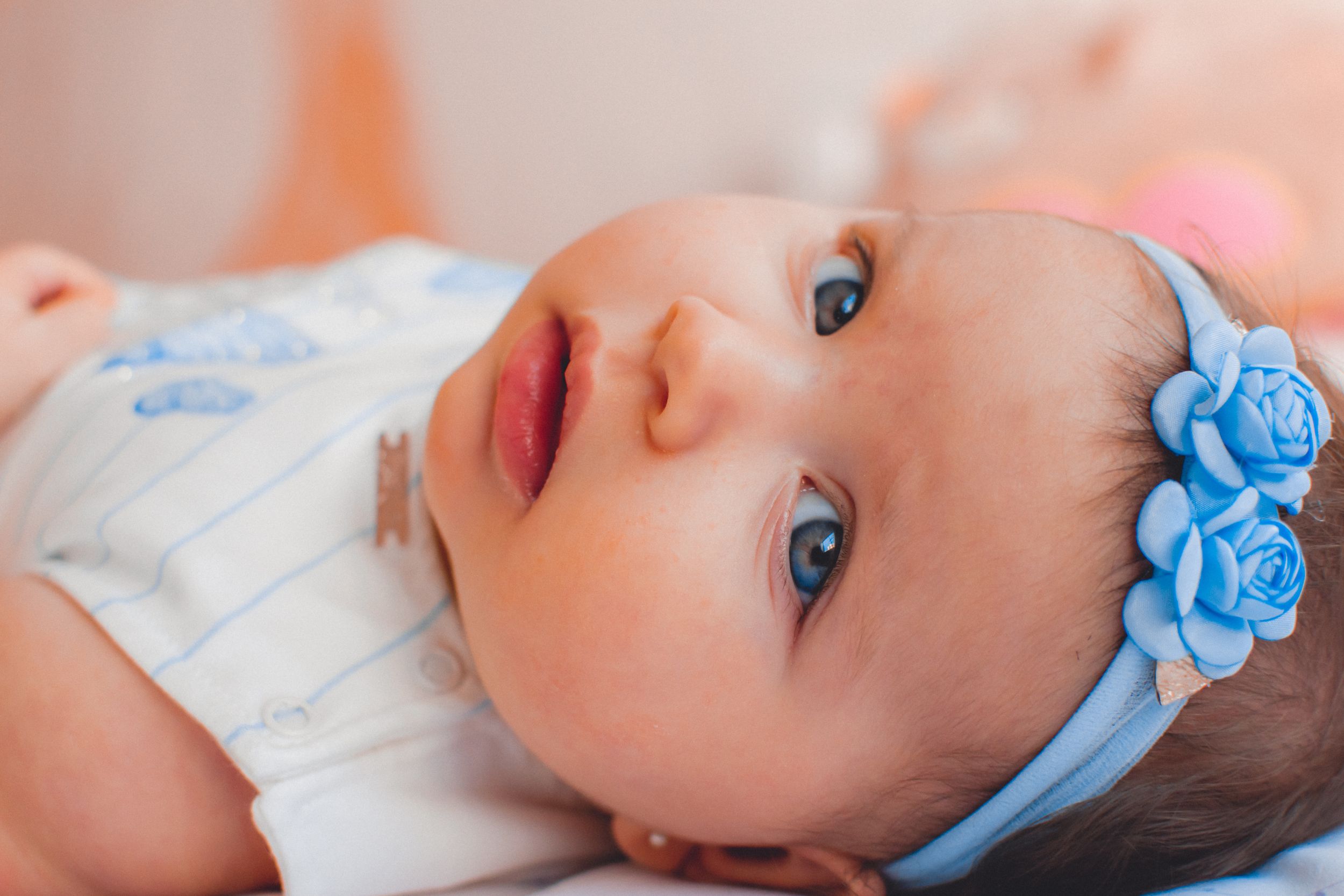 Infant wearing blue floral headband gazes upward with bright expressive eyes.