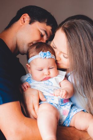 Intimate family portrait with baby in blue floral outfit being embraced by parents.