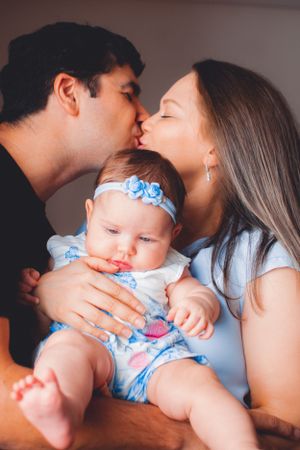 Sweet family moment with baby in blue floral outfit being kissed by parents.